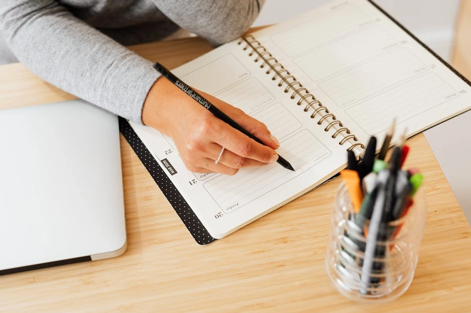 A person writing in a budget planner notebook with a cup of coffee nearby.
